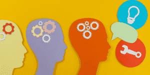 Picture of silhouettes of heads with gears communicating with each other in a yellow background.
