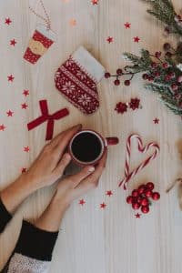 Christmas ornaments are on the floor and there is a hand holding a red cup of coffee