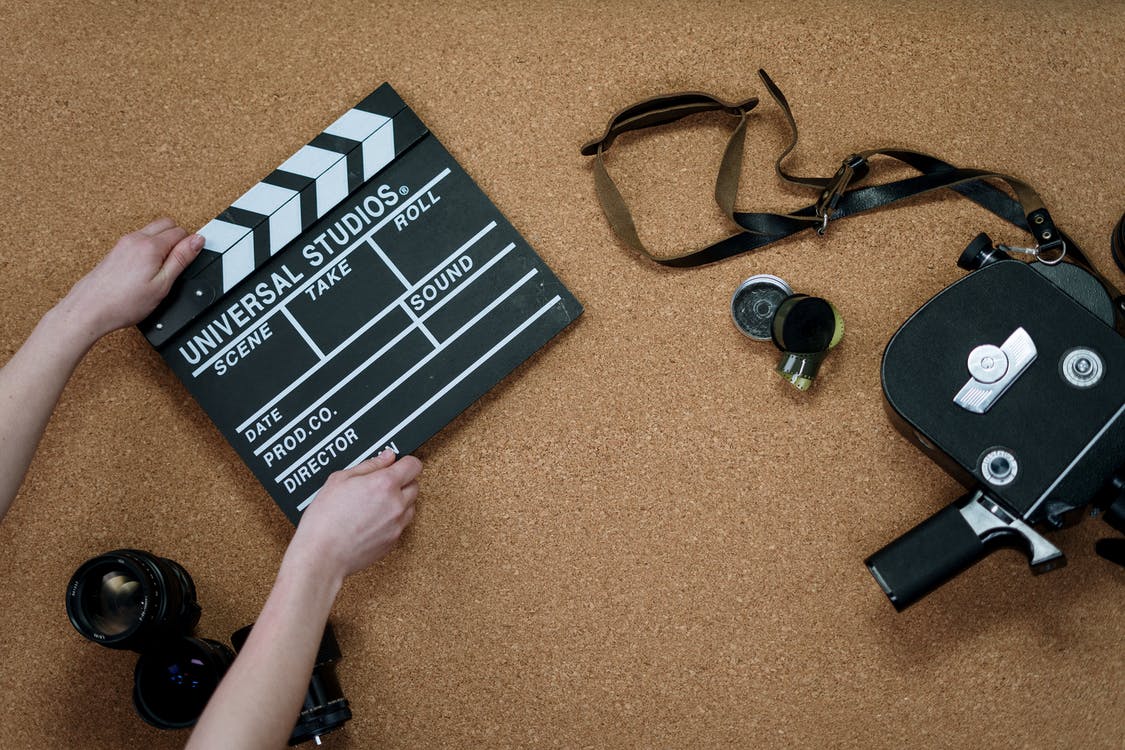 A hand is holding a clapperboard and a camera is beside it.